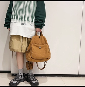 Detail view of a camel canvas backpack featuring a front snap pocket and side pouches