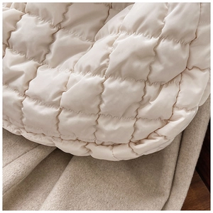 Detail of soft quilted down fabric on cream puffy bag with large diamond stitching