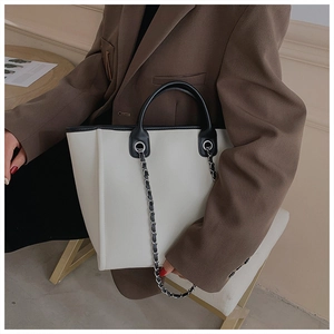 Detail of cream tote bag with black contrast trim and decorative metal chain strap