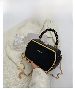 Detail of black curved box handbag with gold metal frame and rope handle on white suit