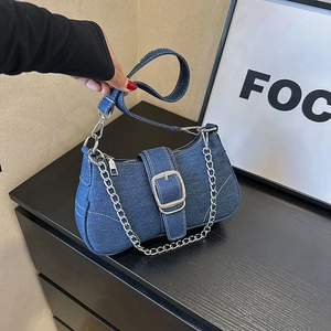 Blue denim crossbody bag with large silver buckle and detachable chain strap on black wood