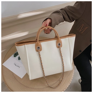 Detail of beige canvas tote with brown leather trim and metallic chain shoulder strap