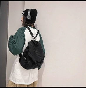 Side view of black canvas backpack with multiple zippers and metal hooks on model
