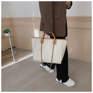 Lifestyle shot of a large beige canvas tote bag with brown leather trim and chain strap