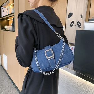Blue denim crossbody bag with silver buckle and chain detail worn by model in cafe