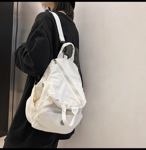 Detail view of white canvas backpack featuring diagonal zippers and adjustable straps