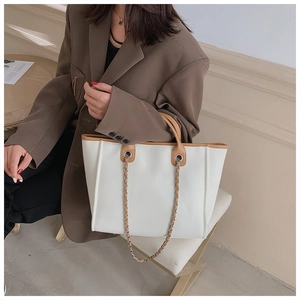 Close-up of minimalist white tote bag with brown leather trim and metal chain straps