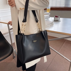Black leather tote bag with gold chain straps and logo patch shown on a model