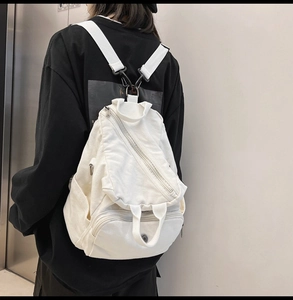 Detailed view of white canvas backpack featuring unique asymmetric 3D zipper pocket