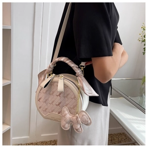 Detail of beige round crossbody bag with scarf-wrapped handle and cute puppy charm