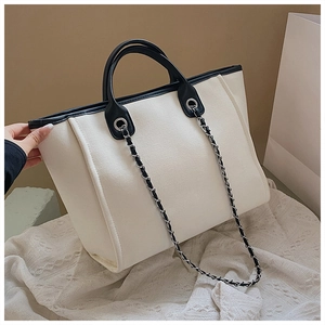 Detail of canvas tote bag with black leather trim and metal chain shoulder strap