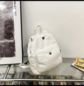 Detail of white canvas backpack front pocket with metal magnetic buckle closure