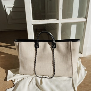Minimalist beige bucket tote bag with black leather trim and chain strap on blazer