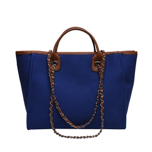 Blue canvas tote bag with brown leather trim and silver metal chain strap on white background