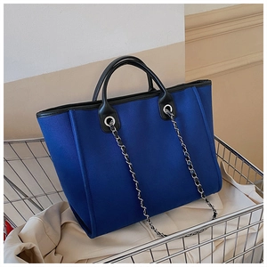 Detail of blue canvas tote bag featuring black leather handles and silver chain straps