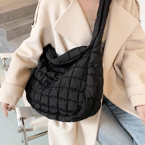 Quilted black puffer shoulder bag with large capacity worn by a model in a trench coat