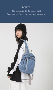 Detail of blue denim mini backpack with light grey fabric straps and zipper pockets