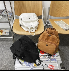 Detailed view of three canvas backpacks in white, brown, and black with flap designs