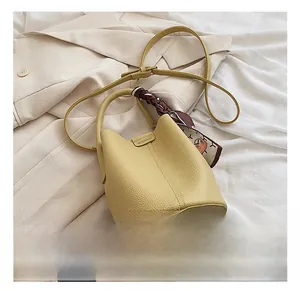 Detail of yellow lychee grain leather bucket bag with decorative silk scarf and metal logo