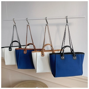Detail of canvas tote bags in navy and cream with leather handles and chain straps