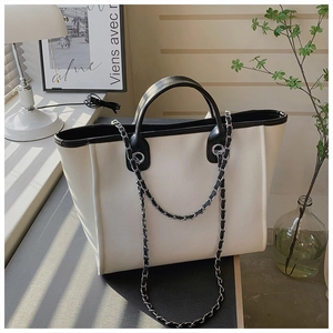 Detail of a large beige tote bag with black trim and elegant chain strap in soft sunlight