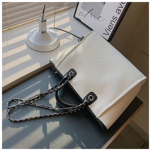 Detail of cream tote bag with black trim and silver chain strap in artistic shadow