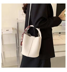 Close-up of beige lychee leather bucket bag featuring decorative silk scarf and gold hardware