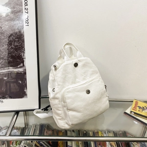 Minimalist white canvas backpack with front pocket and adjustable straps in home setting