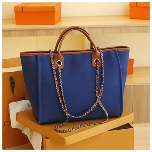 Detail view of the blue canvas tote bag with brown leather trim and chain shoulder strap