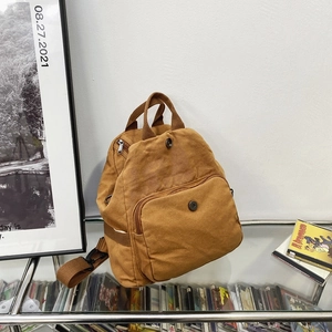 Minimalist tan washed canvas backpack with front flap pocket on a glass display shelf