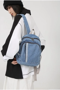 Close-up of a blue denim backpack with a vertical zipper pocket and gray webbed straps