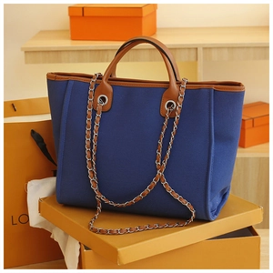 Detail of blue canvas tote bag with brown leather trim and metal chain shoulder strap