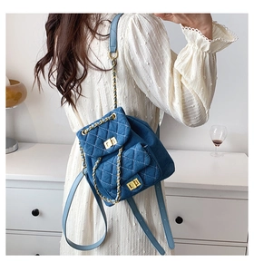 Close-up of blue denim quilted mini backpack with gold chain straps on a white dress