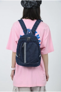 Detail of dark blue washed denim backpack with adjustable straps and front zip pocket