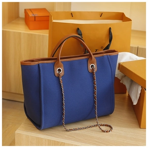 Detailed shot of a blue canvas tote bag with brown leather trim and silver chain strap