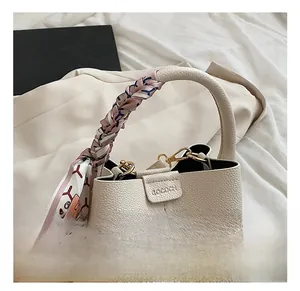 Detail of cream bucket bag featuring a silk scarf wrapped handle and litchi texture