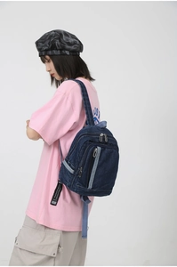 Detail of blue washed denim mini backpack showing vertical zipper pocket and twill texture