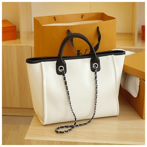 Close-up of cream canvas tote bag with black leather trim and silver chain strap