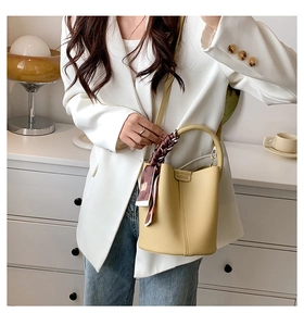 Close-up of yellow lychee leather bucket bag with a decorative silk scarf on the handle