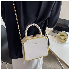 Detail of white octagonal chain bag with gold metal trim and woven handle over black suit