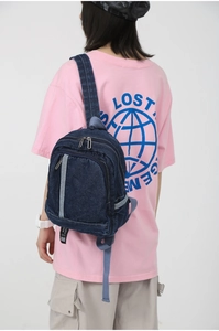 Detail of a dark blue denim mini backpack with zipper pockets on model's back