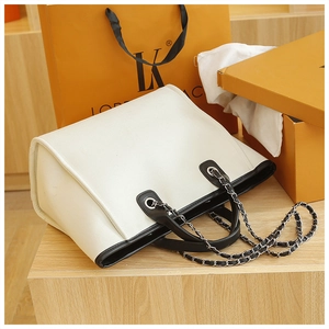 Detailed view of white canvas tote with black leather trim and silver chain shoulder strap