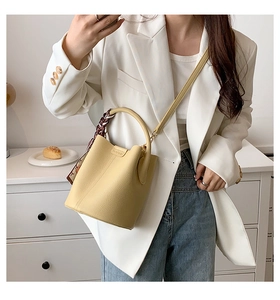 Detail of yellow lychee leather bucket bag featuring a silk scarf wrapped around handle