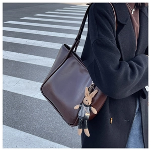 Gros plan d'un sac cabas en cuir marron foncé avec un charm de lapin dans la rue
