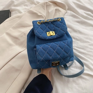 Navy denim quilted backpack with gold chain handle and turn-lock closure on white background