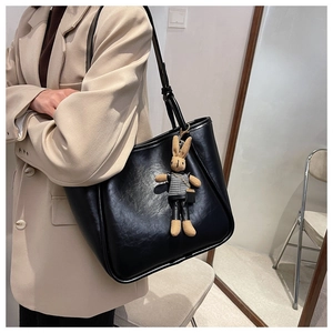 Détail d'un grand sac cabas noir minimaliste avec pendentif lapin sur une tenue beige