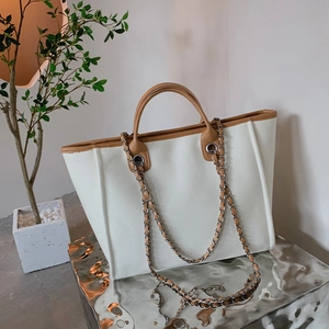 Fashionable canvas and brown leather tote bag with metal chain strap on a display stand