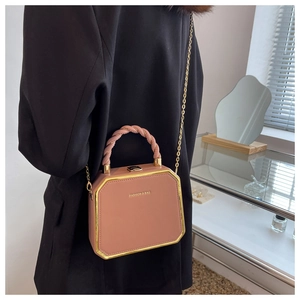 Detail of dusty pink box bag with gold metal trim and woven handle on black blazer