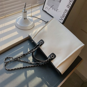Minimalist canvas tote bag with black leather trim and metal chain strap in home setting