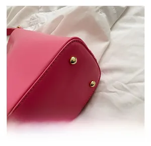 Detail of hot pink tote bag bottom featuring protective gold metal studs and precision stitching